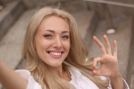 Portrait of a beautiful young blonde woman showing ok sign and smiling.の写真素材