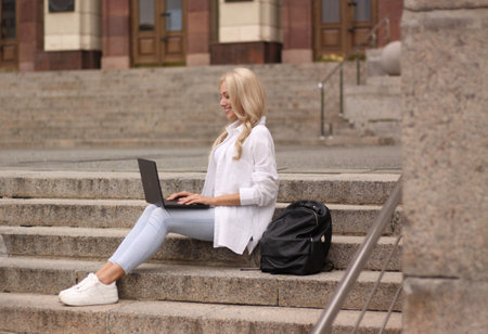 Young woman sitting on steps and working on laptop in the city.の写真素材