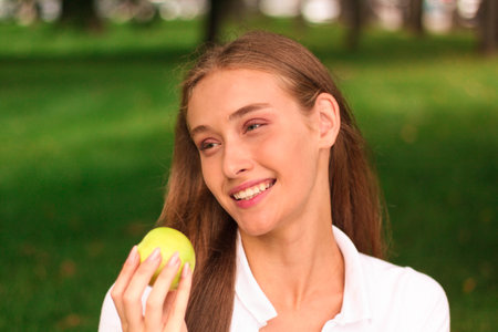 Portrait of a young girl with green apple in the park.の写真素材
