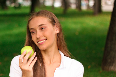 Young woman with green apple in the park. Healthy eating concept.の写真素材