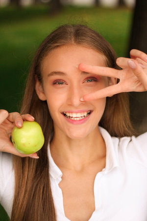 Portrait of a young girl with green apple in the park.の写真素材