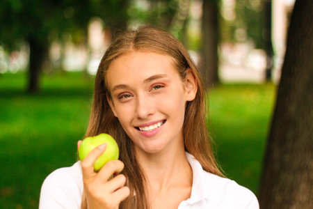 Portrait of a beautiful young woman with green apple in the parkの写真素材