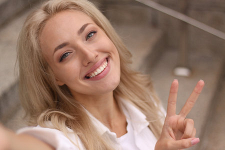 Closeup portrait of a beautiful young blonde woman smiling and showing peace hand sign.の写真素材