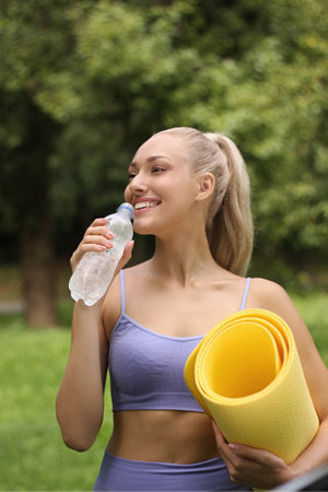 Sporty young woman with yoga mat and bottle of water in parkの写真素材