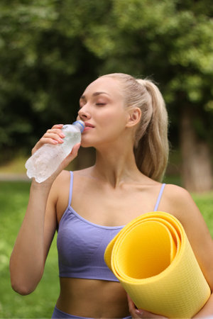 Young woman with yoga mat and bottle of water outdoors on summer dayの写真素材