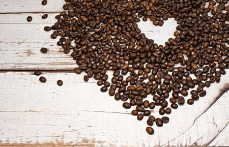 Heart coffee frame made of dark roasted coffee beans on a white wooden backgroundの写真素材