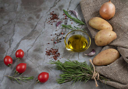 Raw potatoes, rosemary, olive oil, colorful peppers, garlic, onion, fresh and dried tomatoes are the ingredients for delicious baked potatoes in a rustic way. Slightly blurred background with a space for textの写真素材