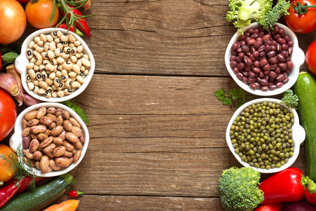 Legumes in bowls and vegetables on a wooden tableの写真素材