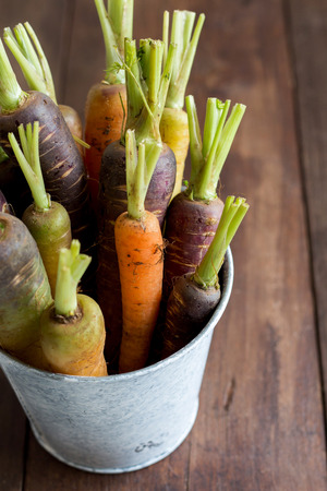Fresh organic rainbow carrots in a bucket on a wooden tableの写真素材