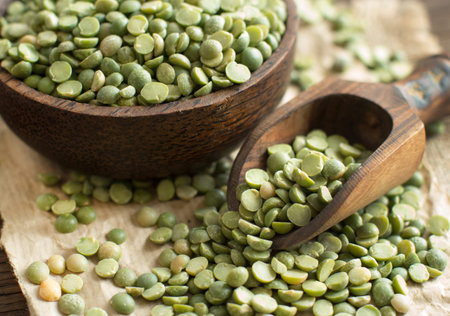 Uncooked Green Split Peas in a bowl  with a spoon on a wooden table