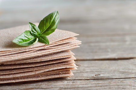 Raw lasagna sheets and basil leaves on a wooden table close up