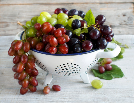 White, red and blue grapes  in a bowl on wooden tableの写真素材