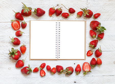 Strawberries and notebook on a white wooden tableの写真素材