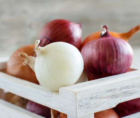 Raw onions in a box on a wooden tableの写真素材