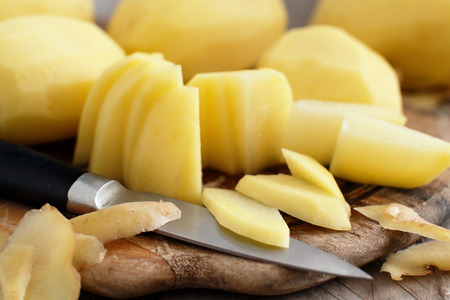 Raw peeled potatoes with a knife on a wooden boardの写真素材