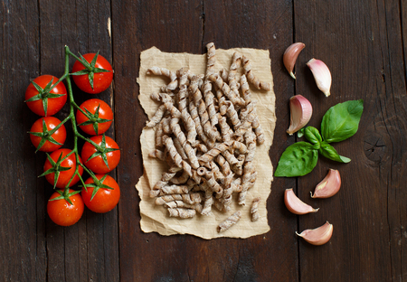 Whole wheat pasta, tomatoes, basil and garlic on a wooden backgroundの写真素材