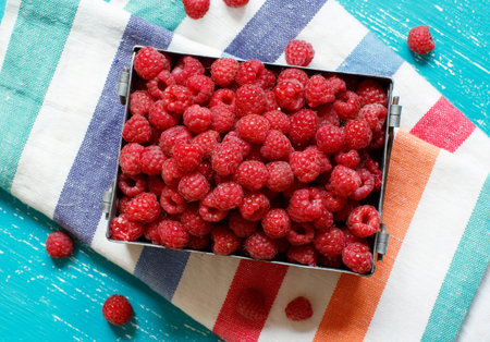 Fresh raspberries in a metal box on a blue background top view