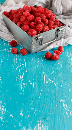 Fresh raspberries in a metal box on a blue background 