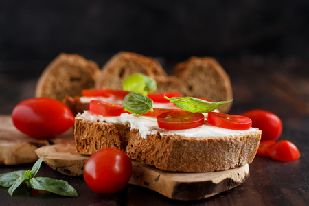 Bruschetta with cream cheese, cherry tomatoes and basil on a wooden tableの写真素材