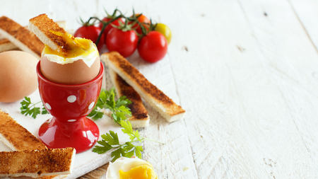 Soft-boiled egg with toasts and tomatoes on a white wooden tableの写真素材