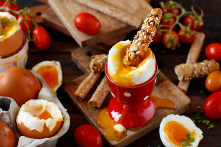 Soft-boiled egg with crisp bread and tomatoes on a wooden tableの写真素材