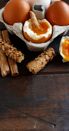 Soft-boiled egg with crisp bread and tomatoes on a wooden tableの写真素材