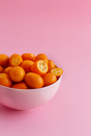 Kumquat fruits in a bowl on a pink background close upの写真素材