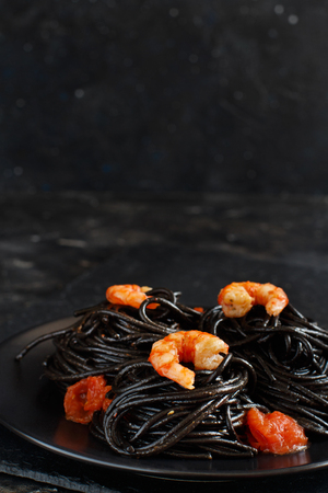 Squid ink black spaghetti with prawns and tomatoes close upの写真素材