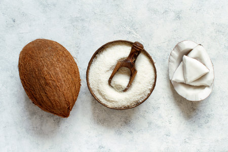 Coconut flour in a wooden bowl with a whole coconut and pieces on a wooden table top view
