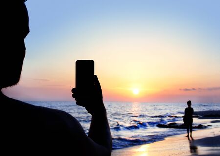 Man takes a sunset photo with his girlfriend on the mobile phoneの写真素材