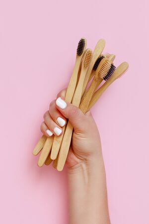 Hand keeps eco friendly bamboo toothbrushes on pink background top viewの写真素材
