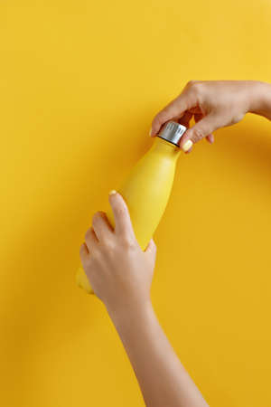 Close up of female hands, opening yellow reusable steel bottle on yellow backgroundの写真素材