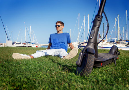 Young Caucasian man sitting outdoor near electric scooter in the marina