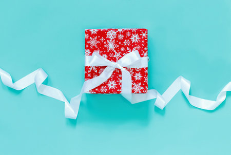 Red gift box with white satin ribbon isolated on light green