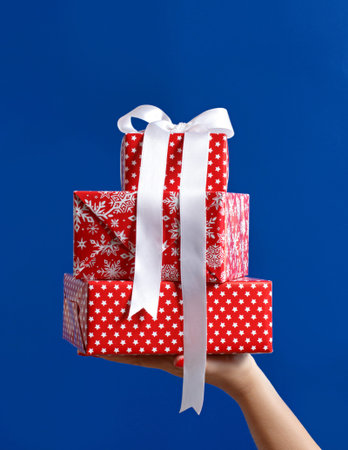 Hand holding red gift boxes close up on blue background