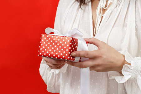 Young woman holding Gift package in hands close up isolated on red