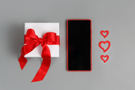 Valentines Day concept - Red Mobile phone, gift box with a bow and hearts top view on a gray backgroundの写真素材