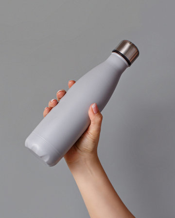Hand with grey rinsulated bottle on grey background. Zero waste, plastic free and sustainable lifestyle conceptの写真素材