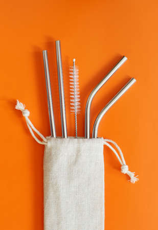 Reusable stainless steel straws and cleaning brush in cream cotton bag on orange background. Eco friendly lifestyle conceptの写真素材