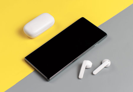 Smartphone and white wireless earphones with the case top view on grey and yellow backgroundの写真素材