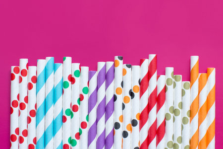 Striped and dotted paper drinking straws on pink background top view. Eco friendly concept