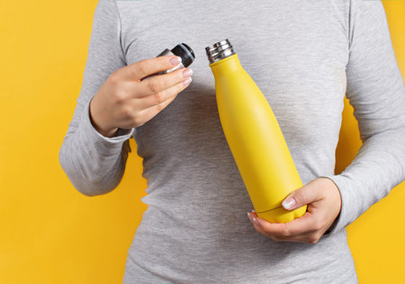 Close up of woman in grey tee holding yellow insulated bottle on yellow background