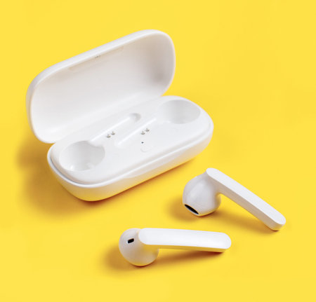 White wireless earphones with case on yellow background close up
