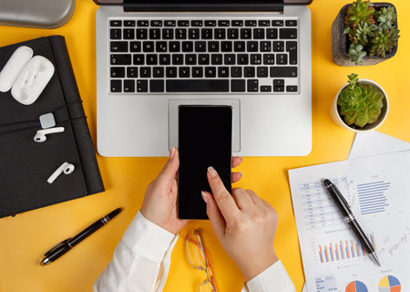 Modern office yellow desk and Business woman hands using smart phone top view