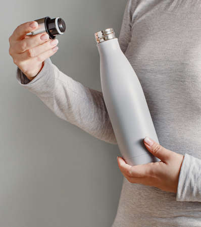 Close up of Woman in grey tee holding grey insulated bottle on grey backgroundの写真素材