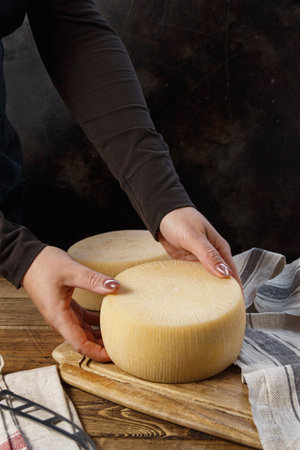 Somebody hands put a wheel of  fresh homemade cheese on a wooden board close upの写真素材