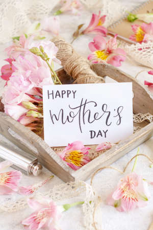Happy Mother's Day handwritten card on a wooden tray between pink flowers close upの写真素材
