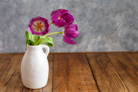 Purple tulip flowers in a vase near the grey wall on a wooden tableの写真素材