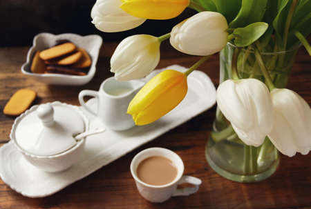 Coffee cup and vase with white and yellow tulips on wooden table close up selective focusの写真素材