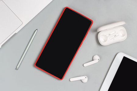 Red Mobile phone, earphones and tablet near laptop on white background